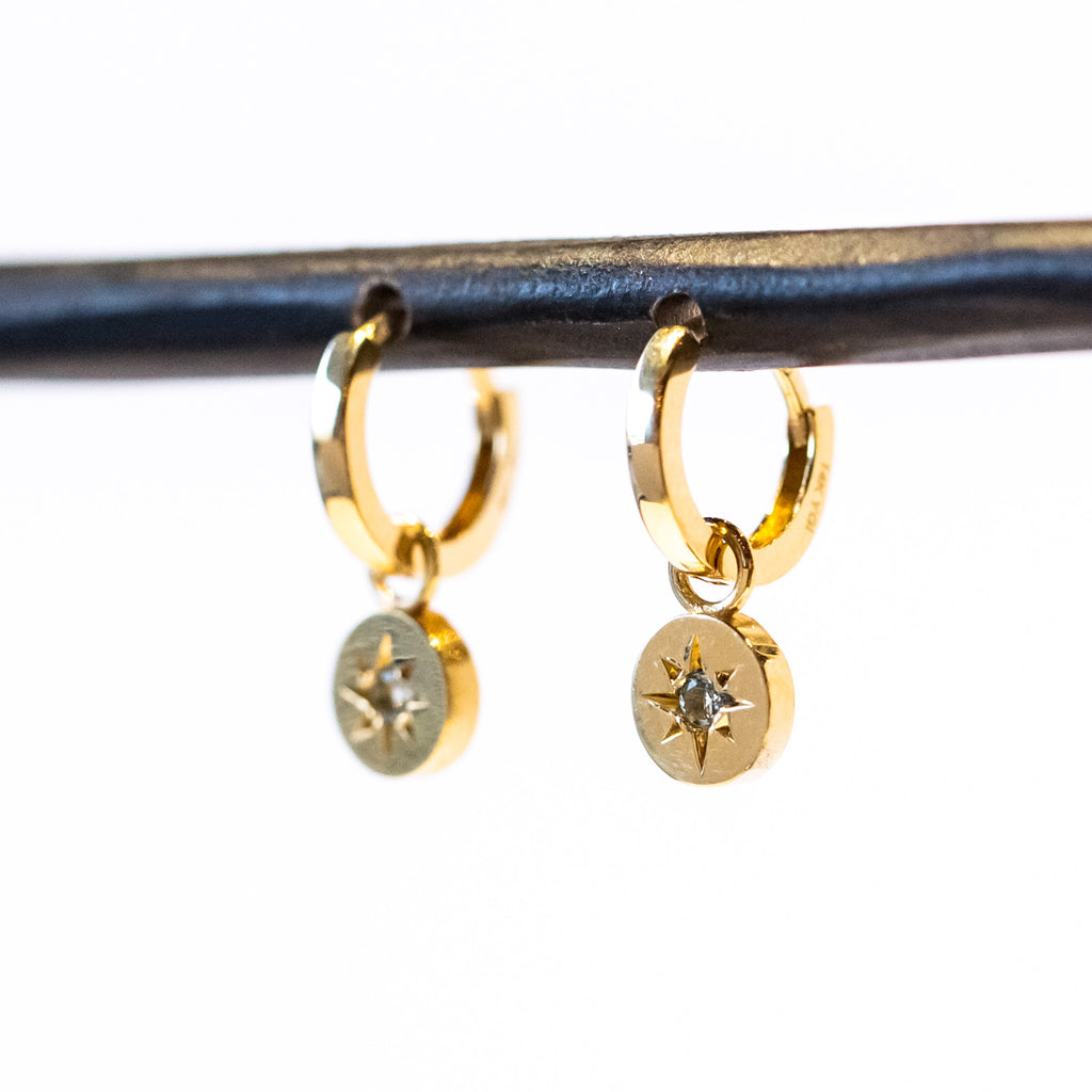 Dainty gold circle drops with a star-set aquamarine gemstone hang from small gold huggie hoop earrings.