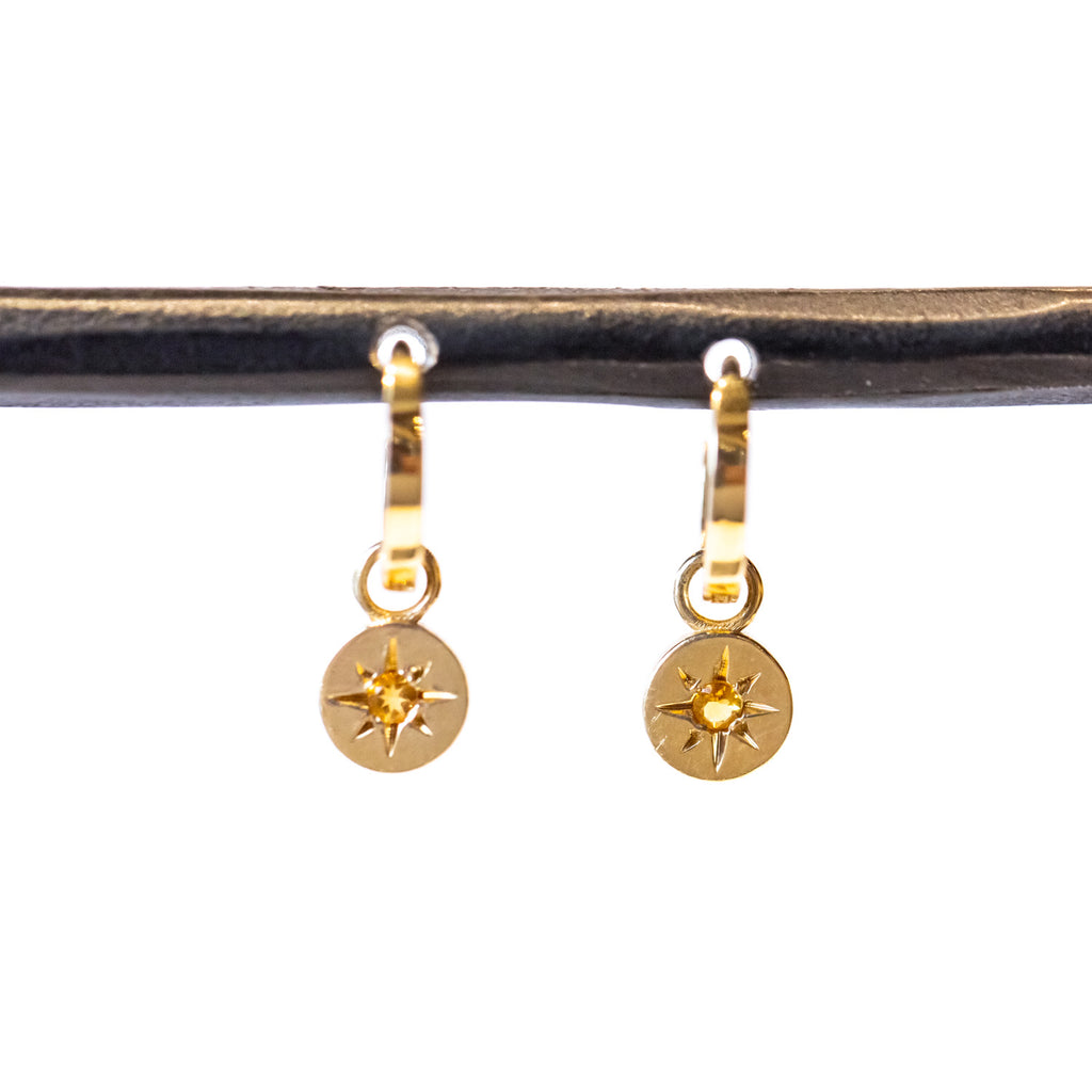 A dainty gold huggie hoop earring featuring a circular drop with star-set citrines at their center.
