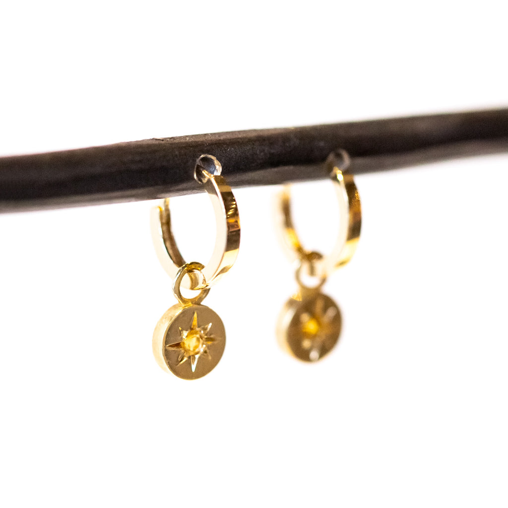 A dainty gold huggie hoop earring featuring a circular drop with star-set citrines at their center.