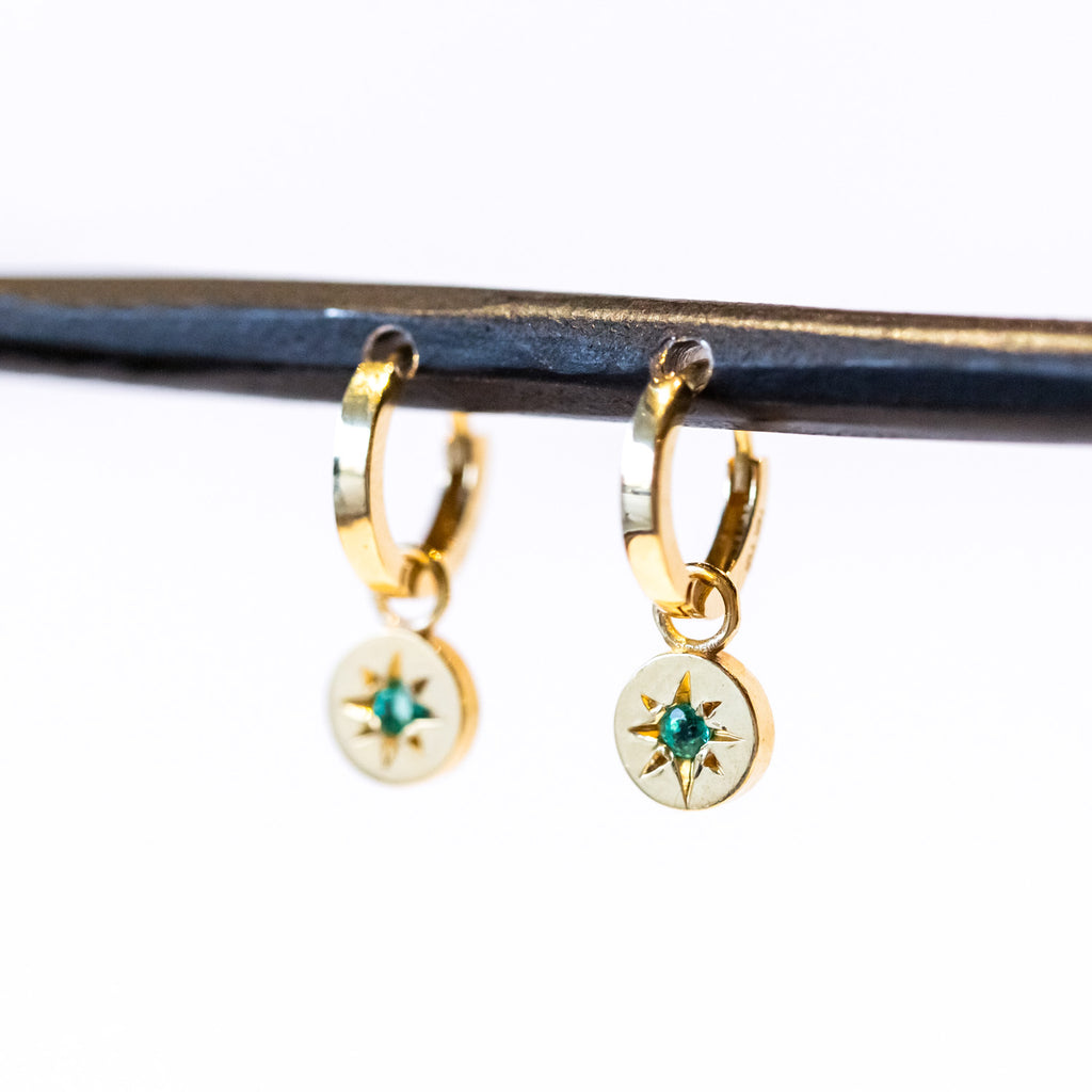 Dainty yellow gold drop earrings featuring small round drops with star-set emeralds hanging from huggie hoop earrings.