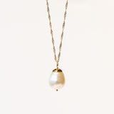 A white baroque pearl drop pendant with a gold bale on a gold chain necklace.