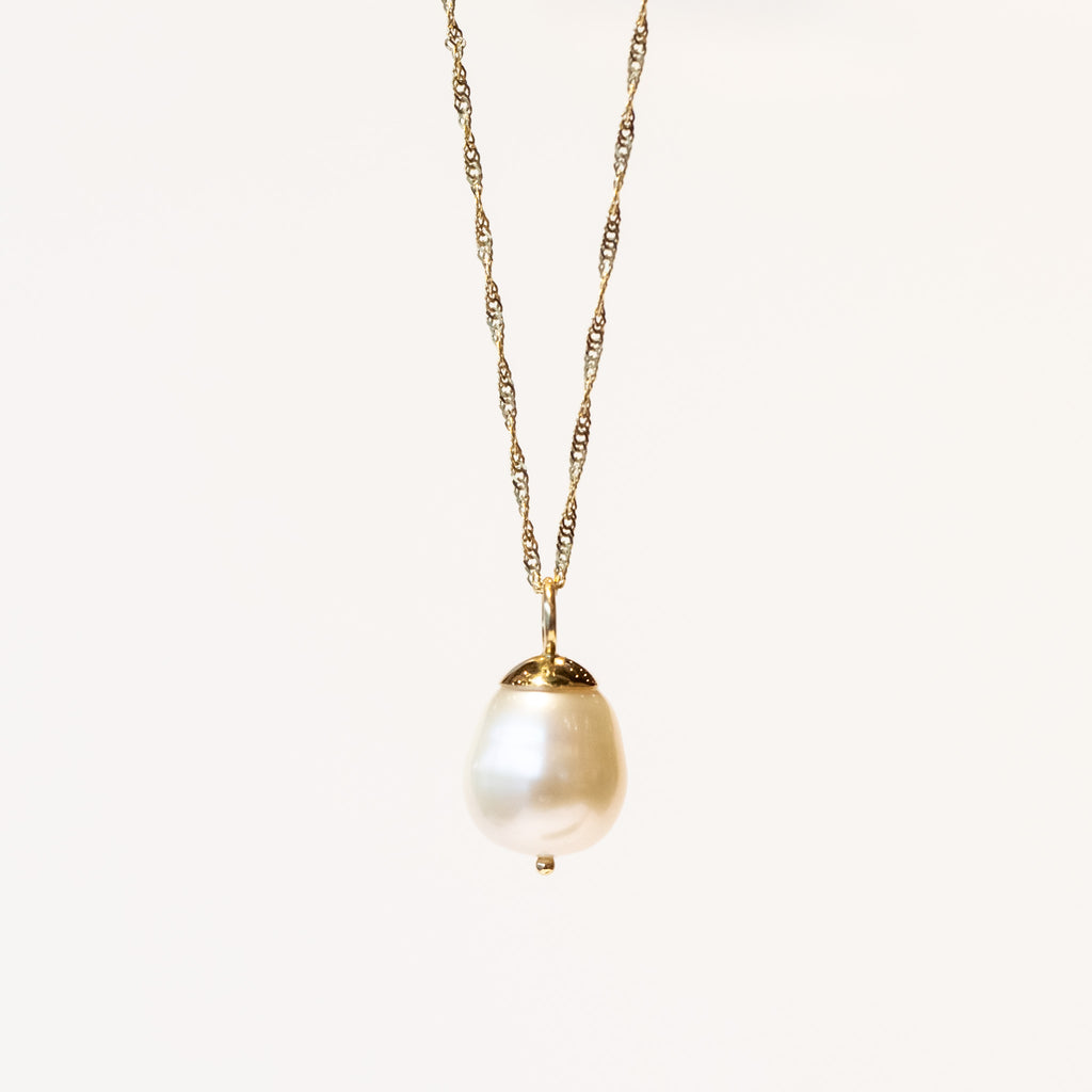 A white baroque pearl drop pendant with a gold bale on a gold chain necklace.