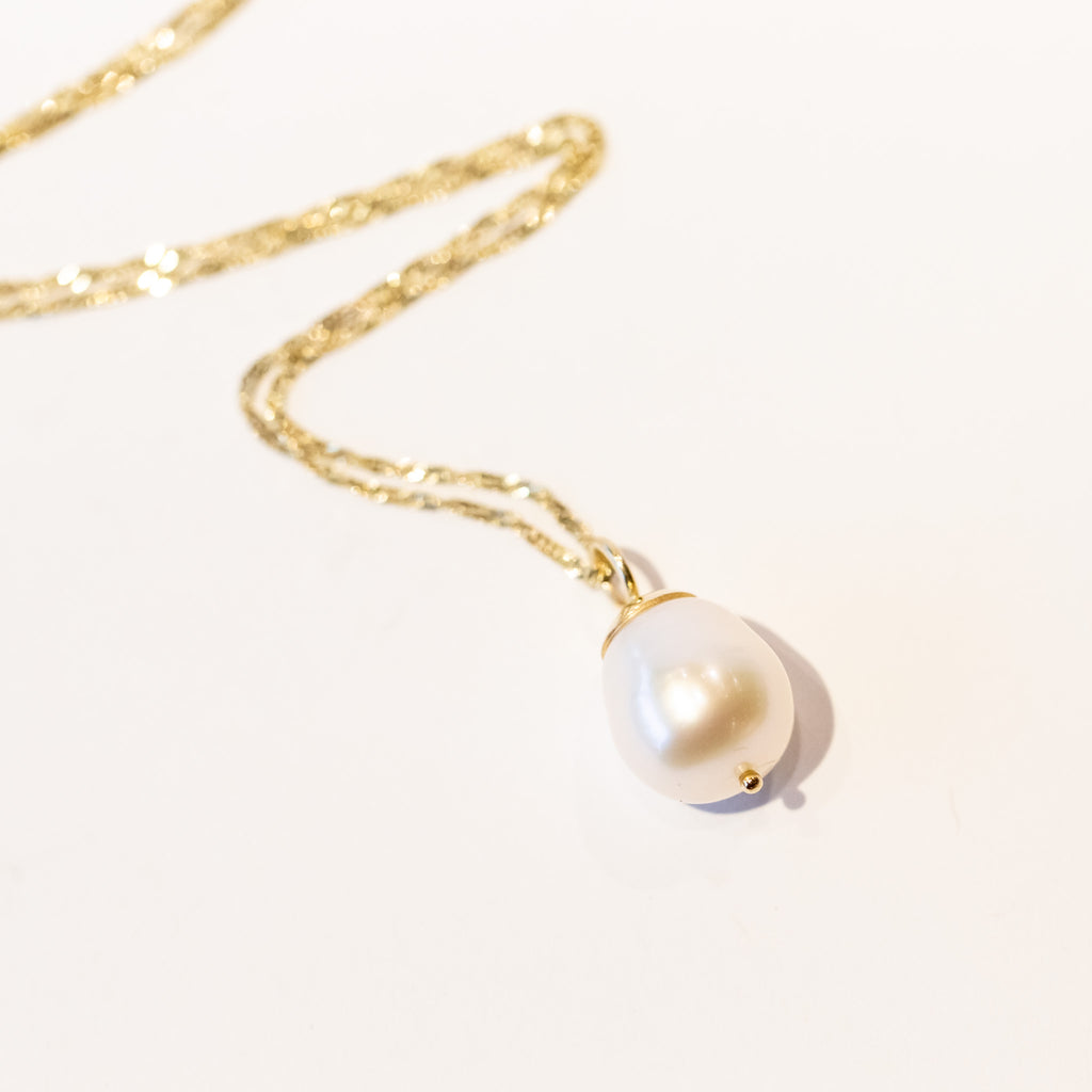 A white baroque pearl drop pendant with a gold bale on a gold chain necklace.