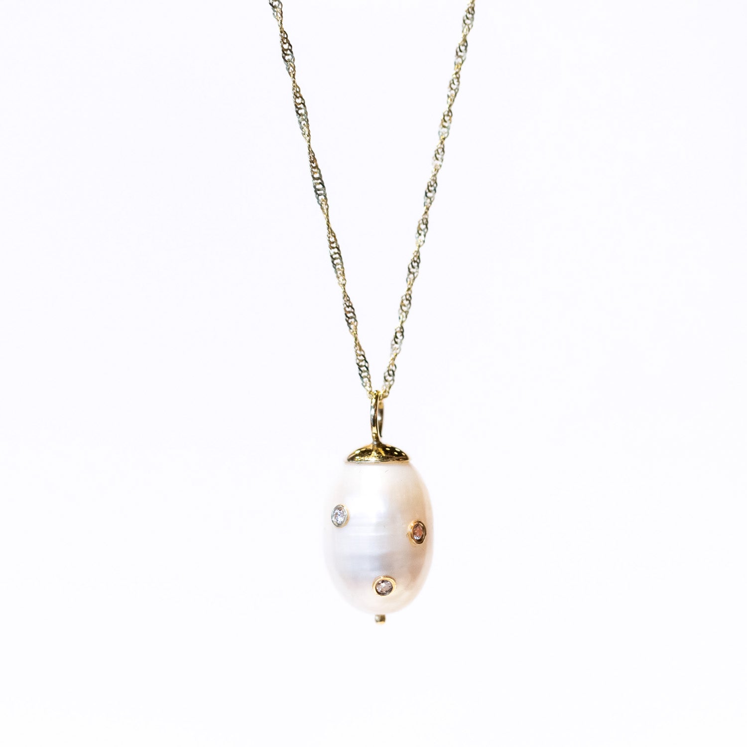 A baroque white pear embedded with three tiny diamonds hangs from a delicate gold chain in this Ariel Gordon pendant.
