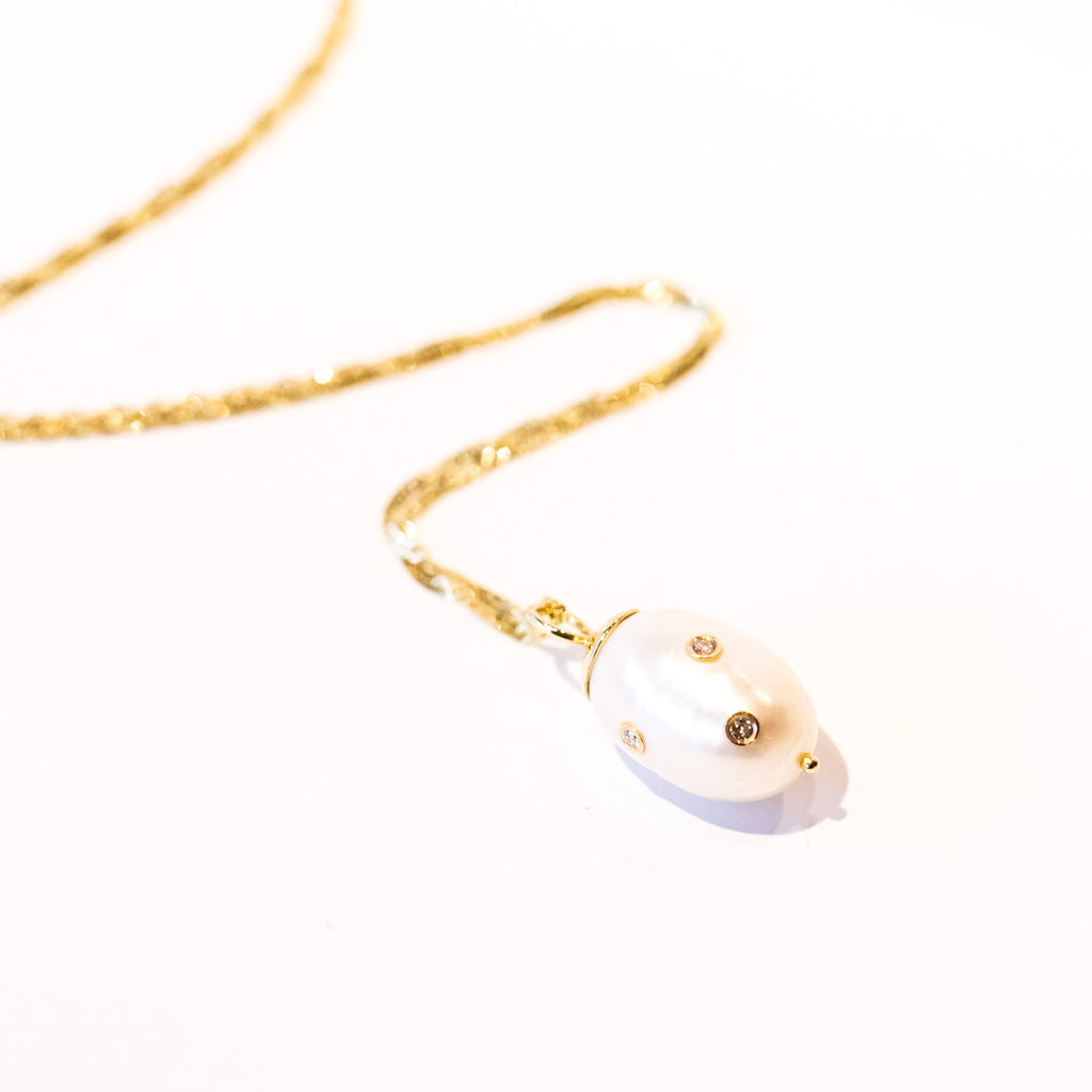 A baroque white pear embedded with three tiny diamonds hangs from a delicate gold chain in this Ariel Gordon pendant.