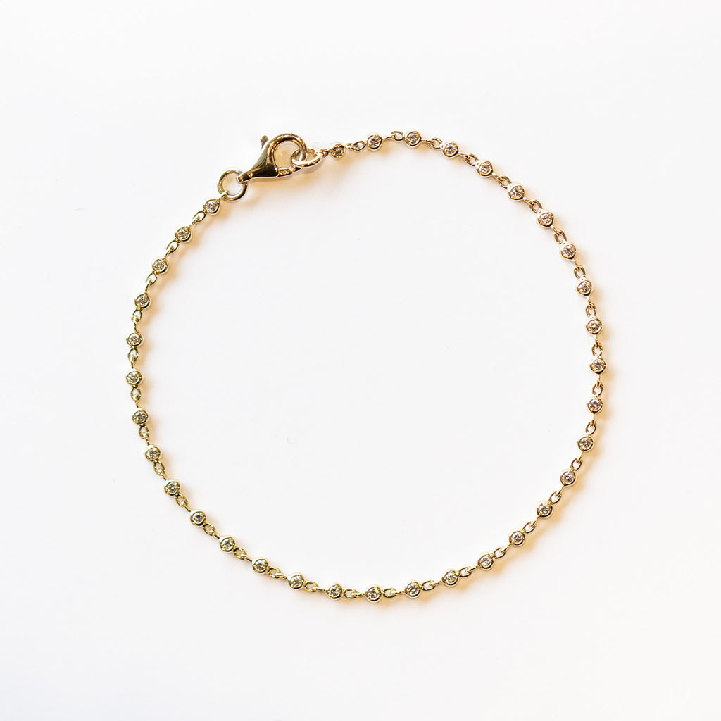 A diamond tennis bracelet made up of round, bezel set diamond links set in yellow gold.