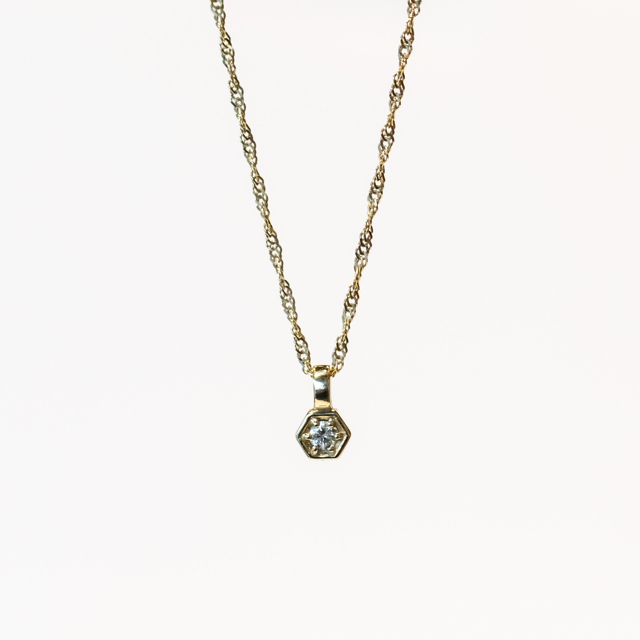 a dainty hexagon shaped pendant set with a round diamond hangs on a delicate gold chain necklace.