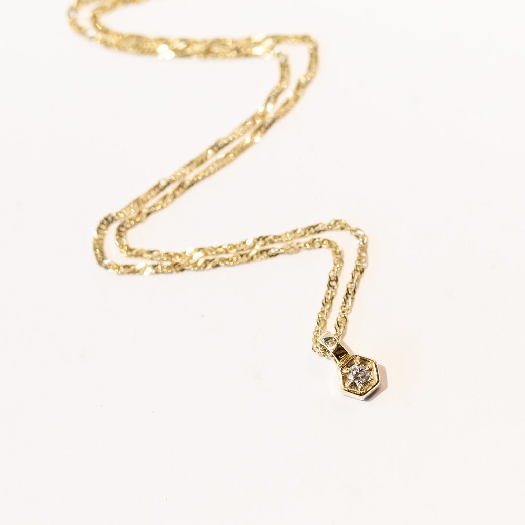 a dainty hexagon shaped pendant set with a round diamond hangs on a delicate gold chain necklace.