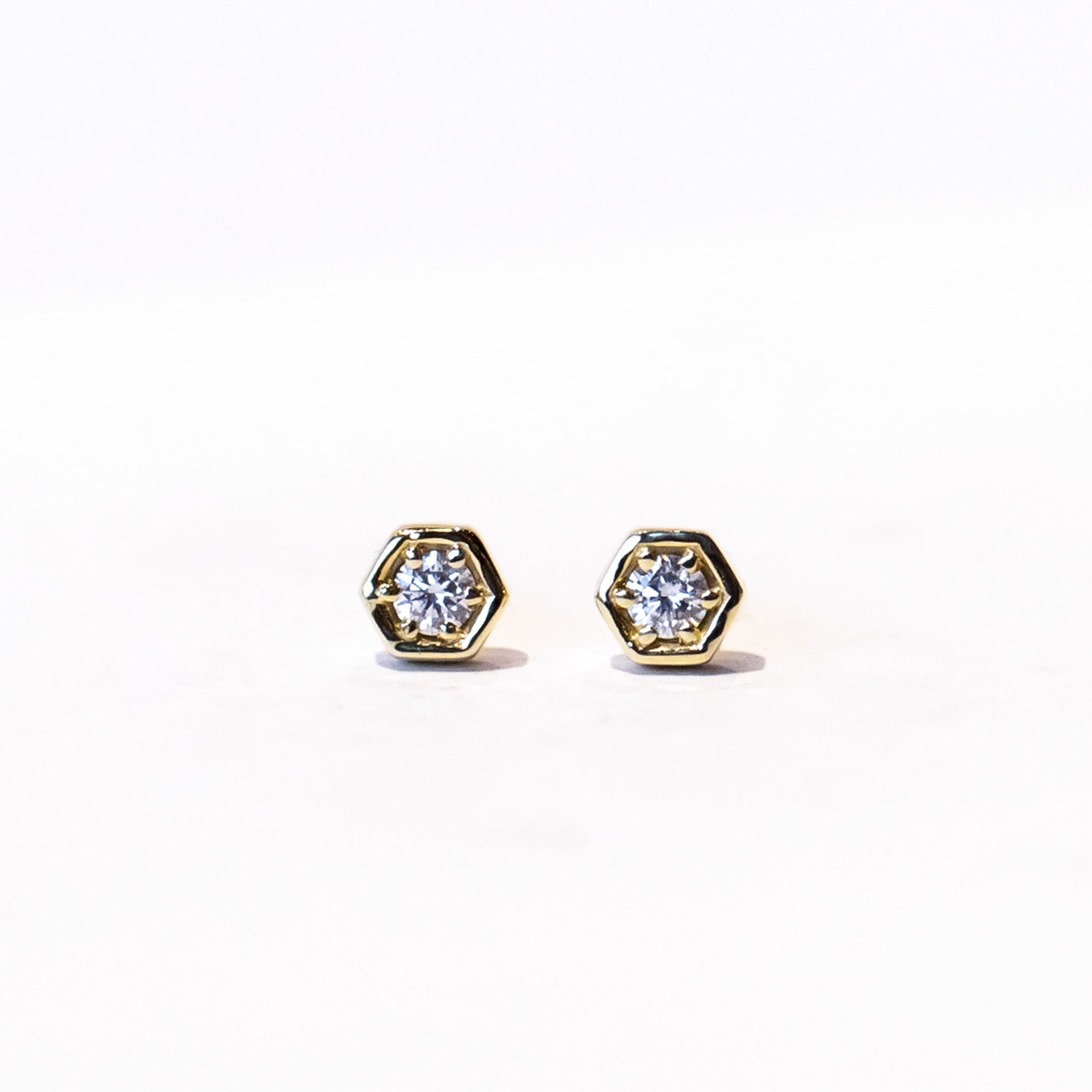 Dainty gold hexagon shaped stud earrings set with a single round diamond.