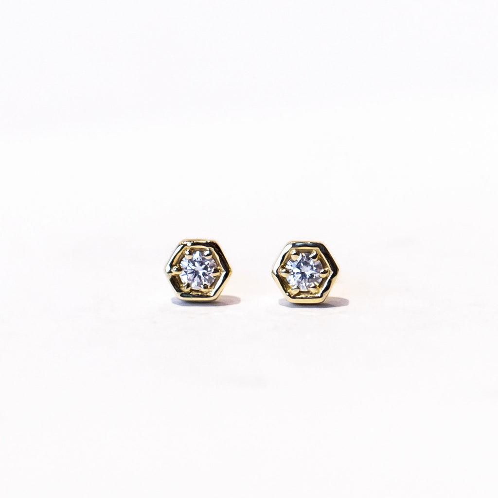 Dainty gold hexagon shaped stud earrings set with a single round diamond.