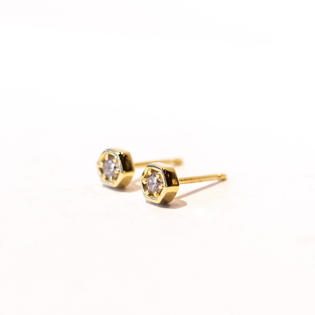 Dainty gold hexagon shaped stud earrings set with a single round diamond.