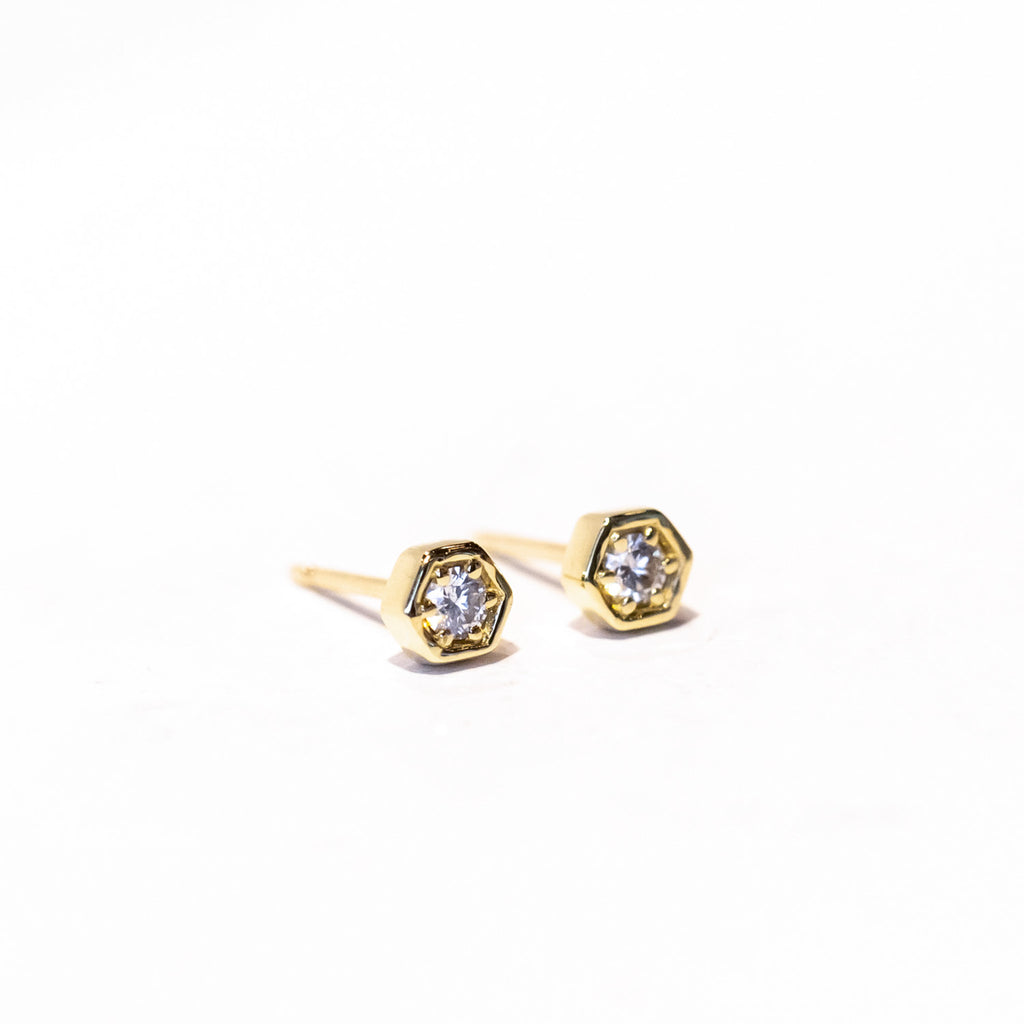 Dainty gold hexagon shaped stud earrings set with a single round diamond.