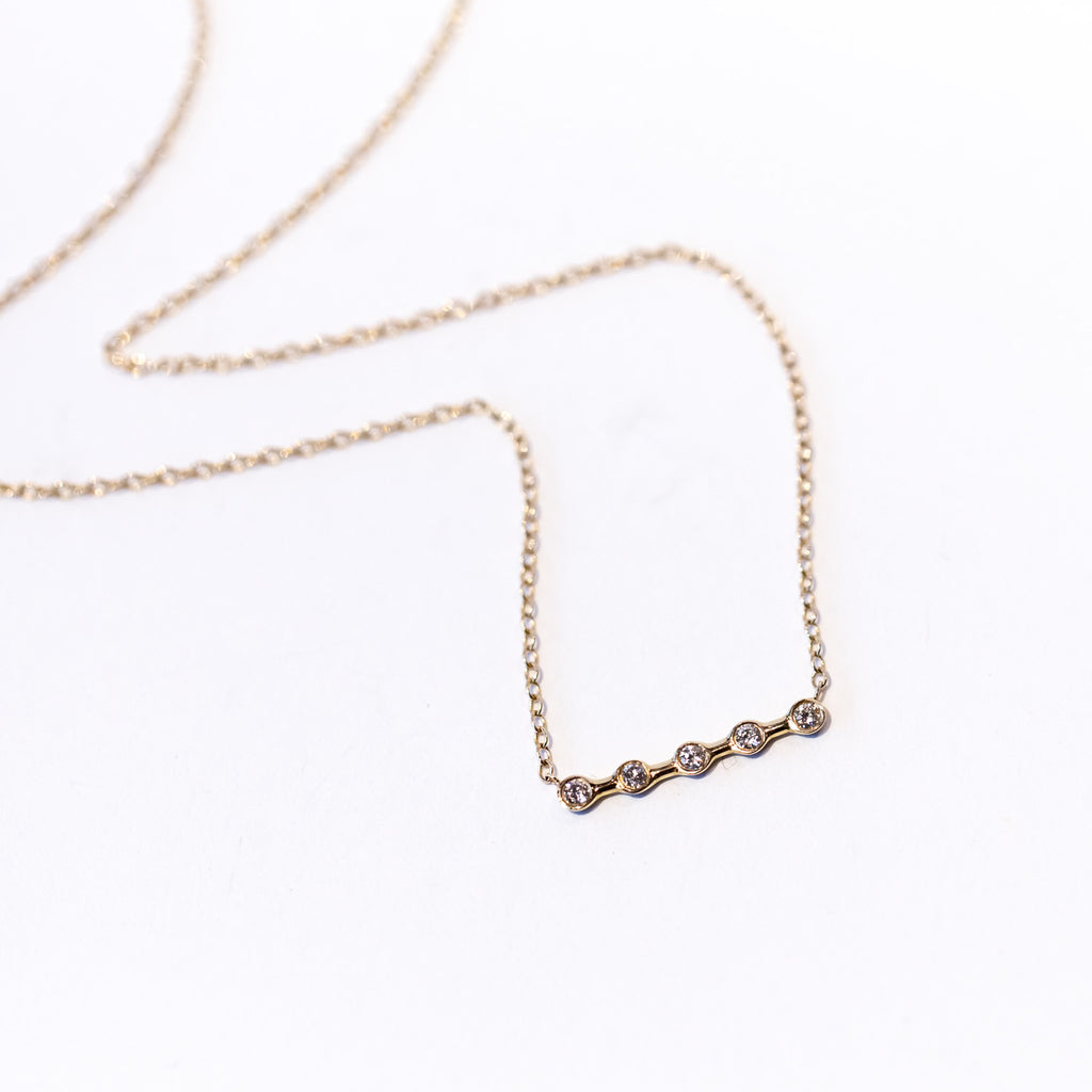 A gold line-shaped pendant featuring five spaced out bezel set diamonds, secured in the center of a classic gold cable chain.
