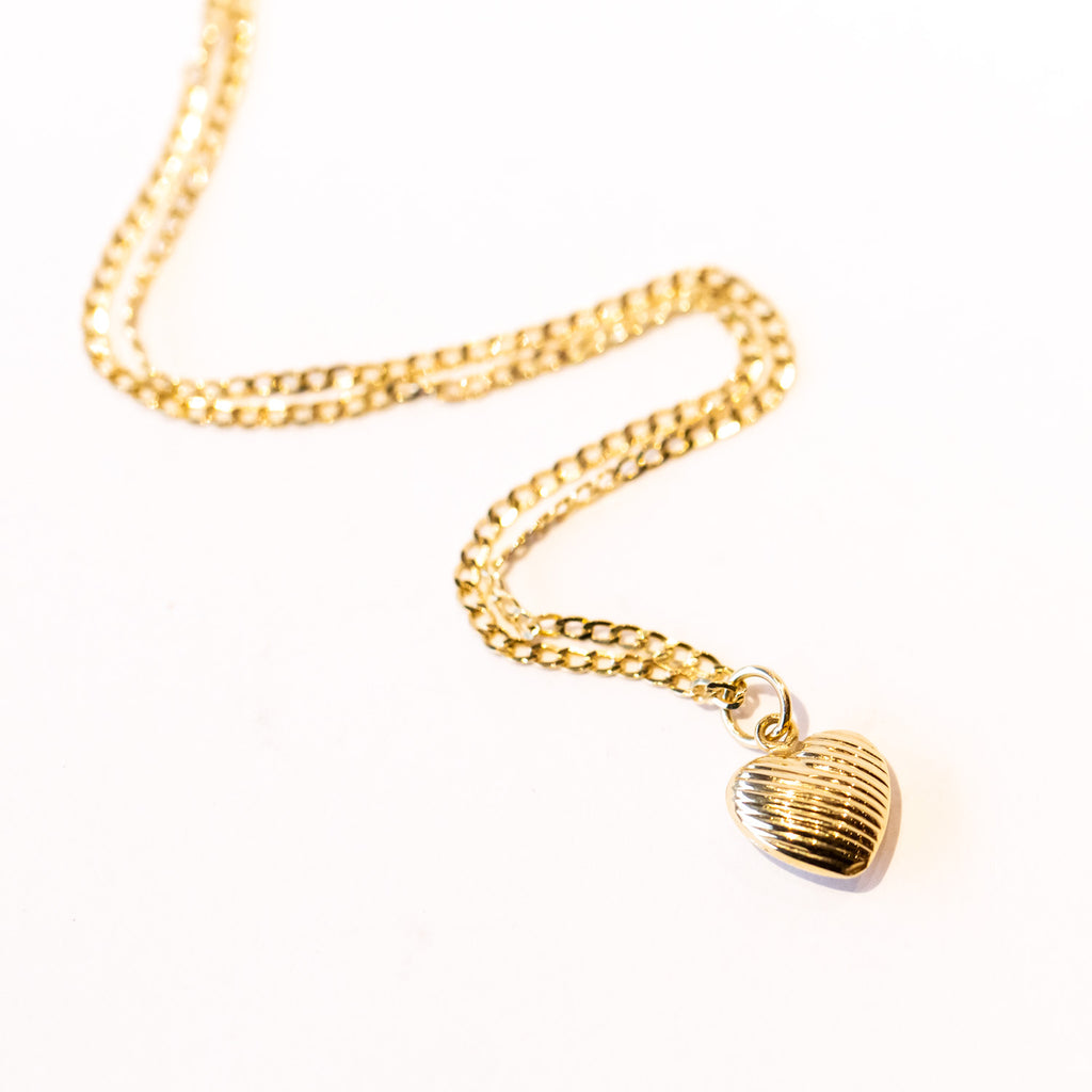 An etched gold heart pendant hangs from a single cuban link chain necklace.