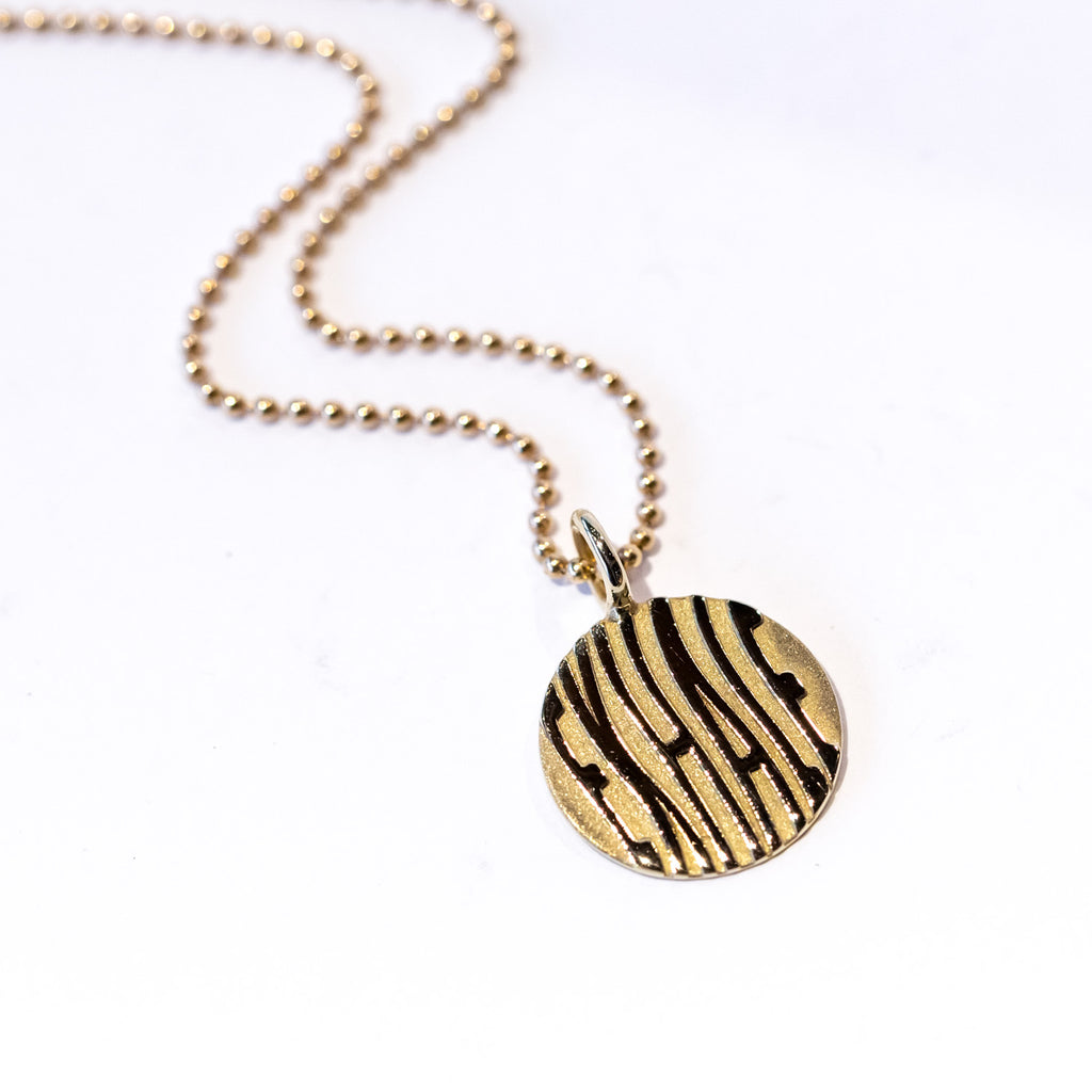 A round gold pendant with etched wavy letters spelling "exhale" hangs from a gold ball chain.