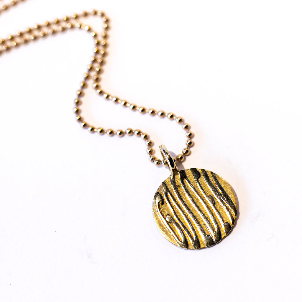 A round gold pendant featuring wavy letters spelling "golden" and suspended from a gold ball chain necklace.