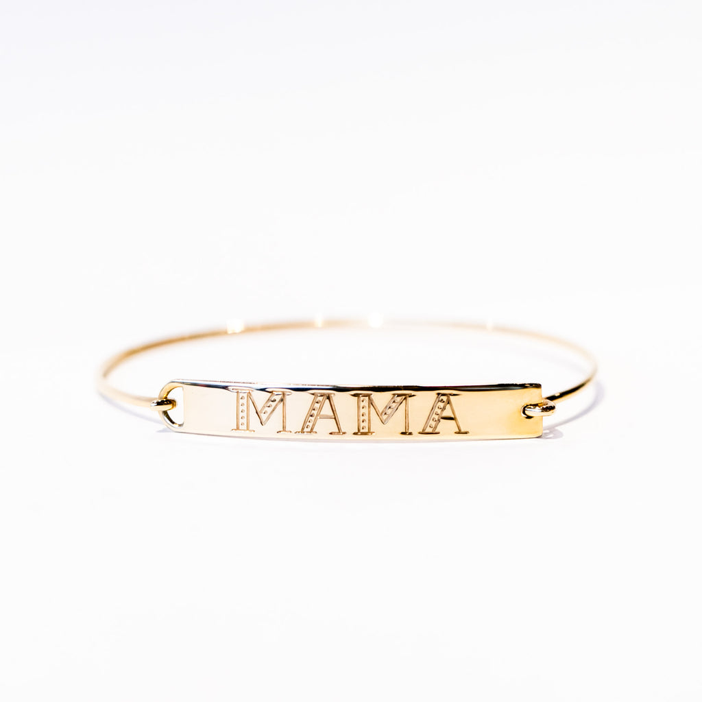 A thin gold wire cuff bracelet with a flat rectangular plate reading "mama" on the front.