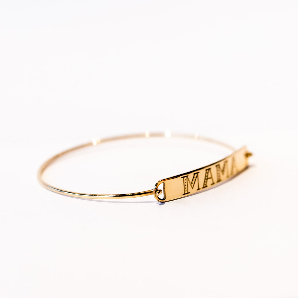A thin gold wire cuff bracelet with a flat rectangular plate reading "mama" on the front.