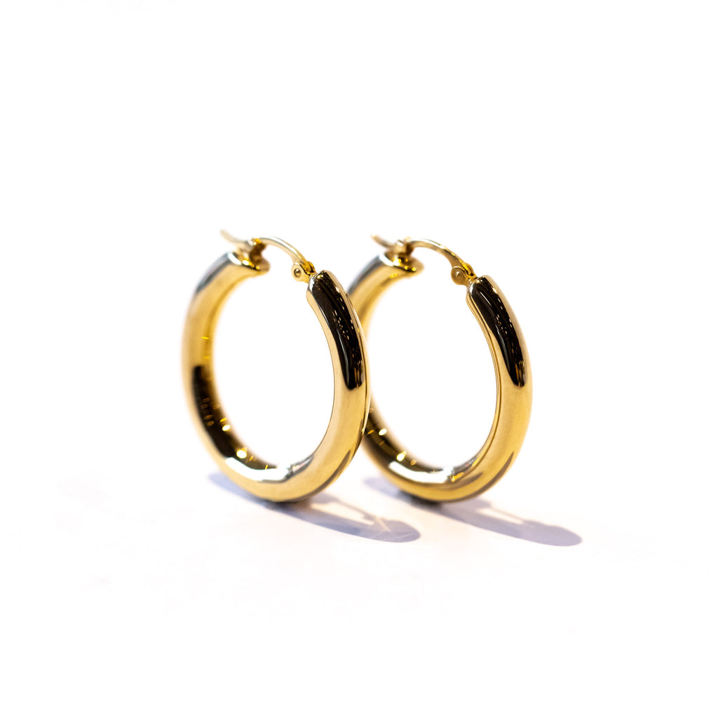 A gold hoop earring with a wide round profile.