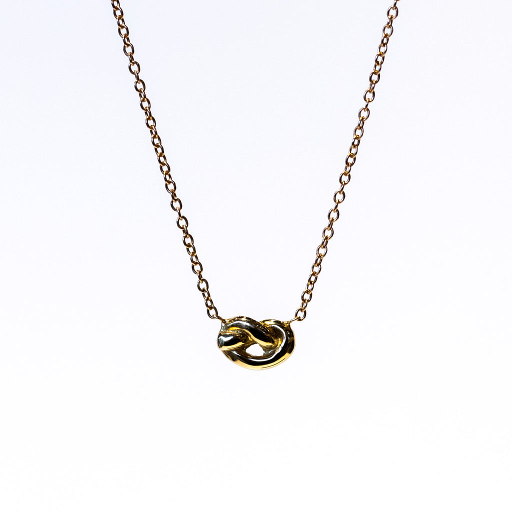 A dainty gold knot is suspended in a classic cable chain necklace.