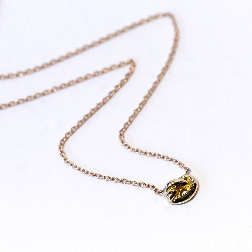 A dainty gold knot is suspended in a classic cable chain necklace.