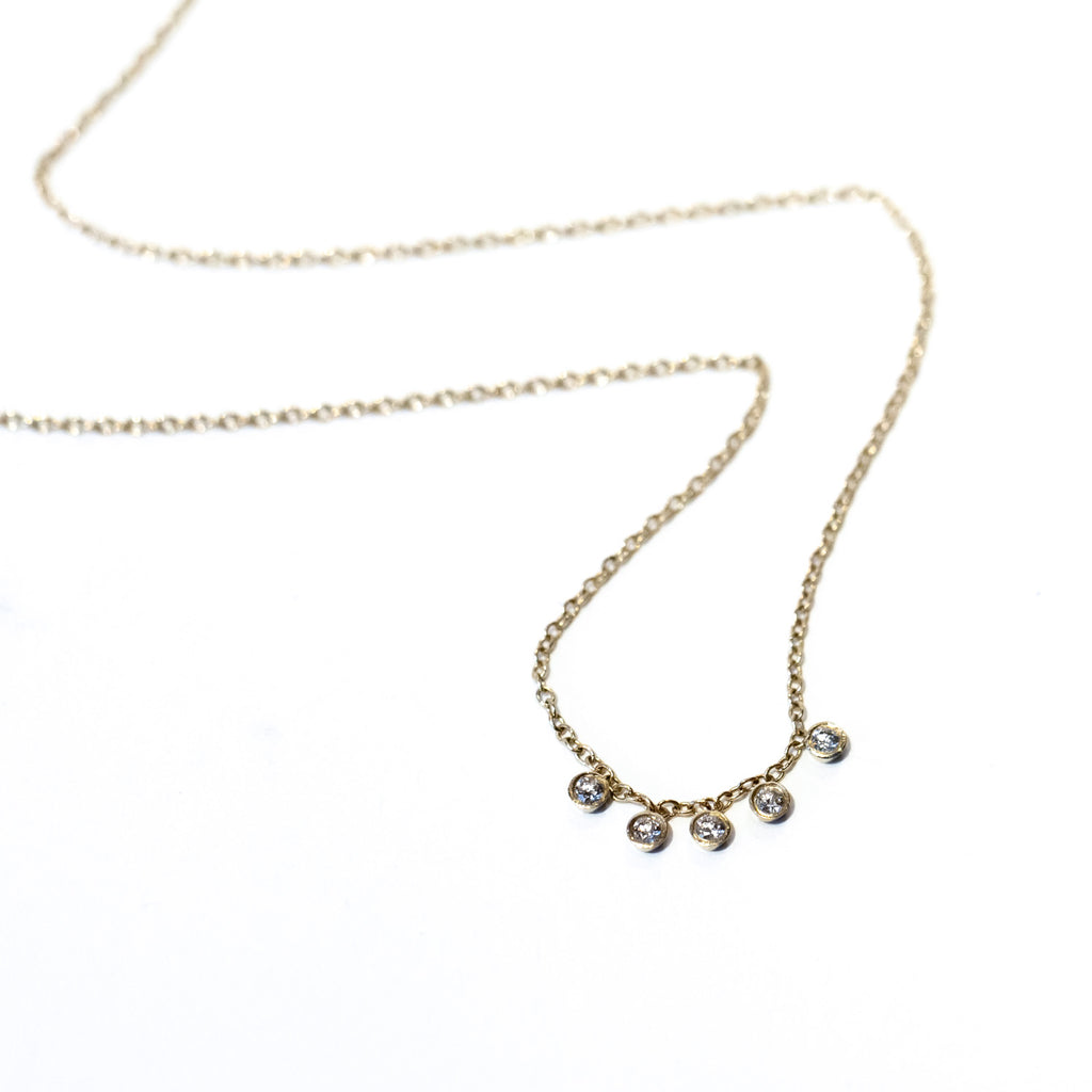 A gold cable chain necklace with five petite, round bezel set diamond dangles stationed at the center.