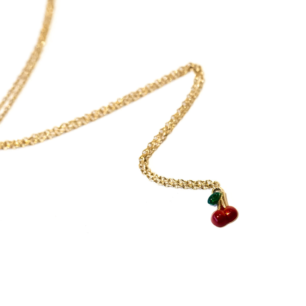 A tiny red enamel cherry charm hangs from a delicate gold cable chain necklace.
