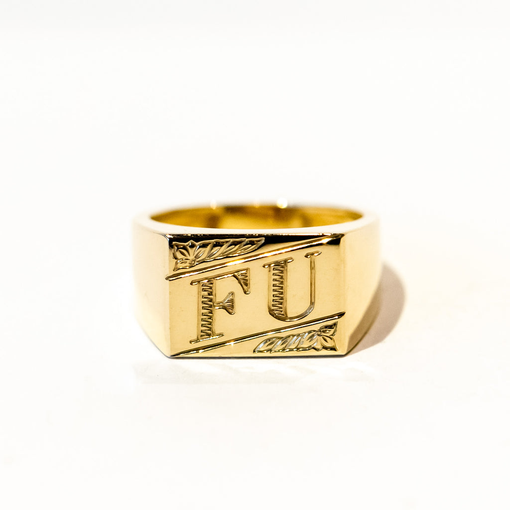 A gold signet ring with an engraved rectangular face that reads "FU"