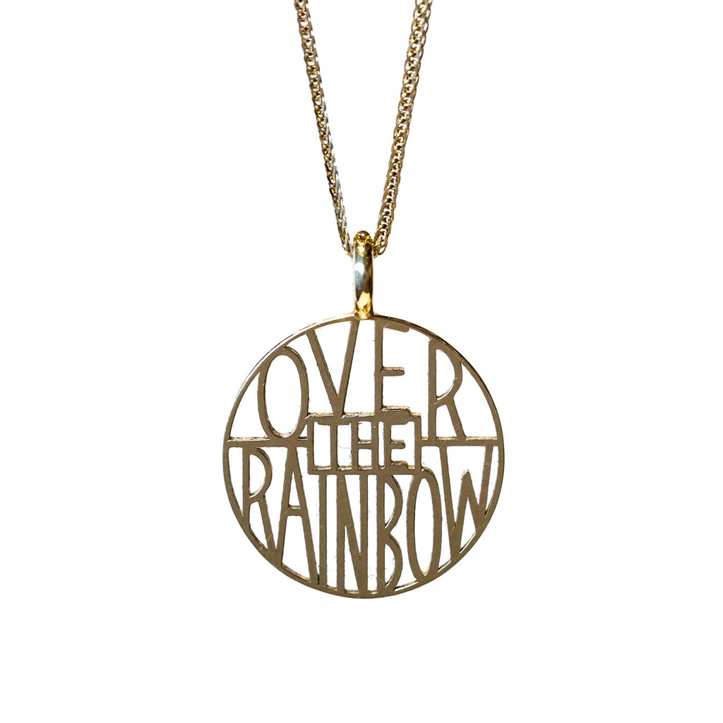 A circular gold pendant with thin lettering reading "over the rainbow".