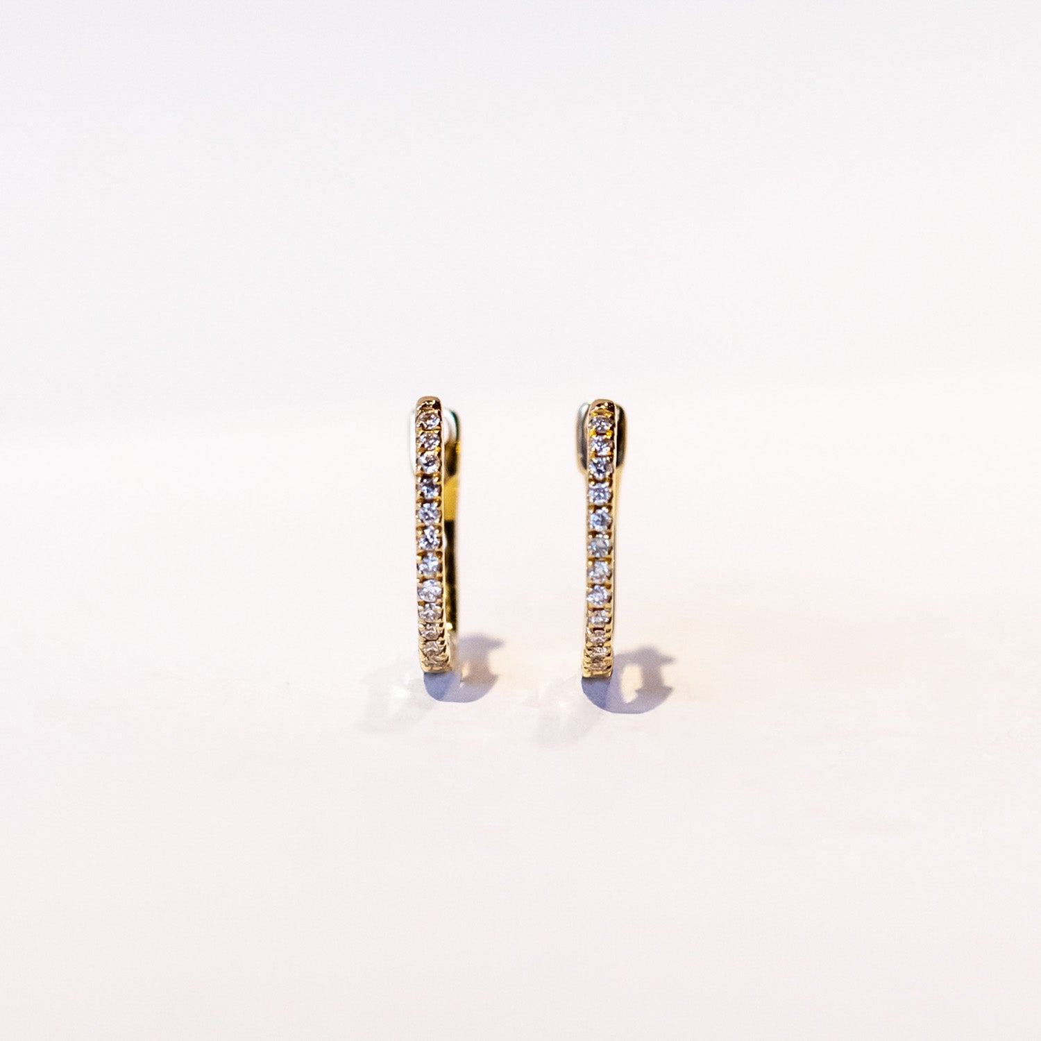 A petite gold hoop earring with a row of round pave set diamonds down the front.