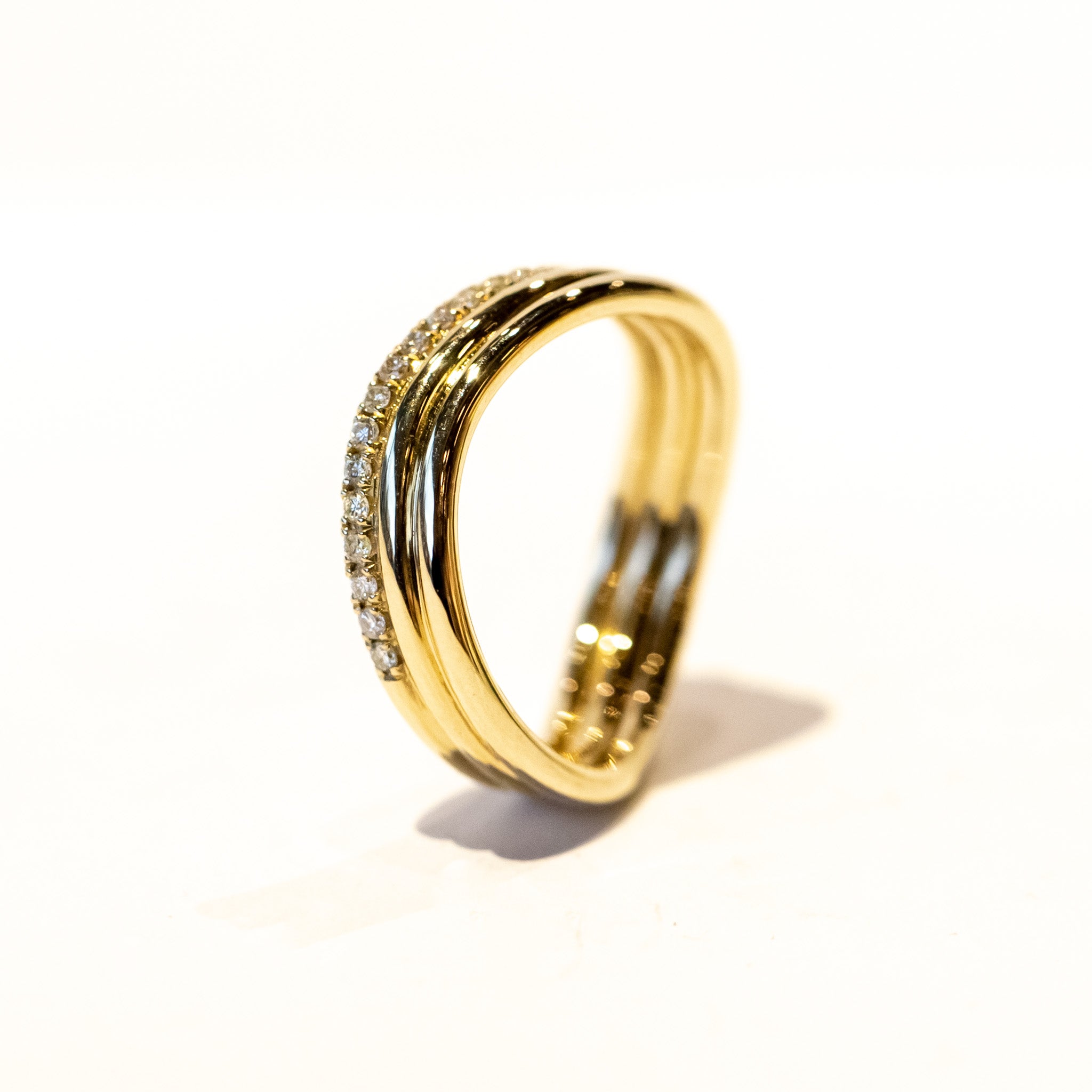 A three-banded wavy gold ring with one of the bands covered in a row of diamonds.