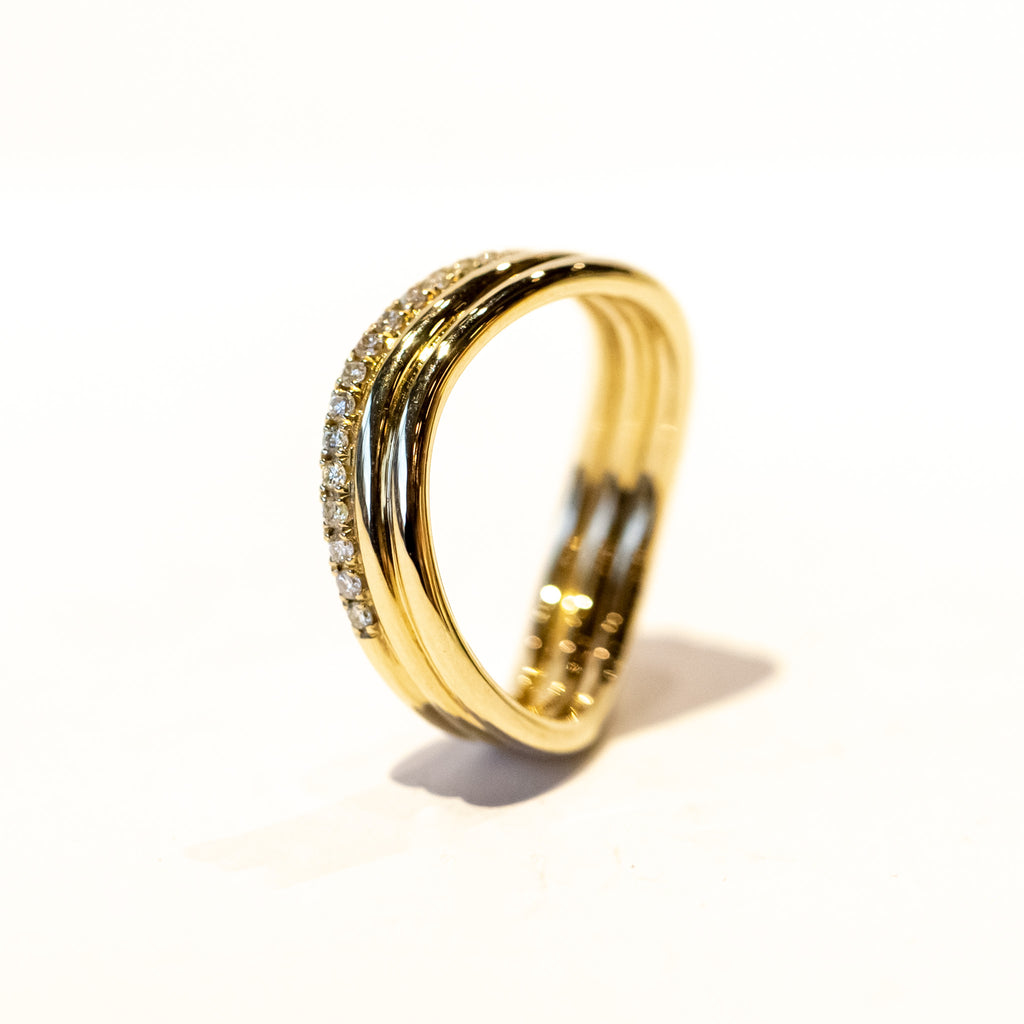A three-banded wavy gold ring with one of the bands covered in a row of diamonds.