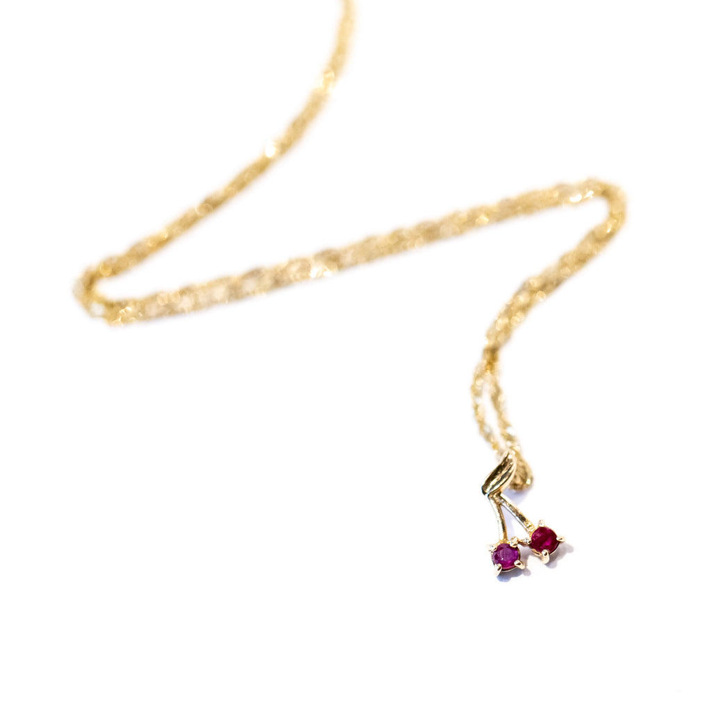 A delicate gold chain necklace with a tiny ruby cherry charm.