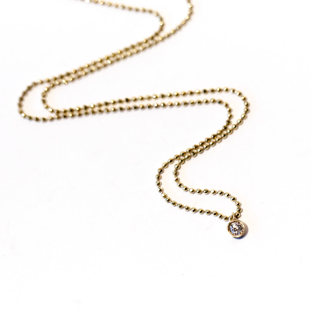 A dainty round bezel set diamond hangs from a delicate gold ball chain in this Ariel Gordon necklace.
