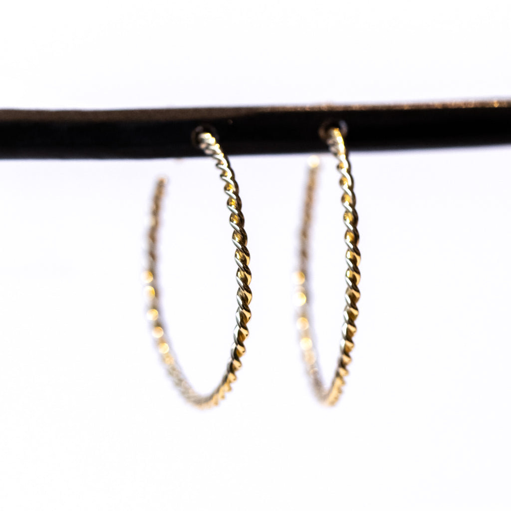 A pair of skinny gold twisted wire hoop earrings.