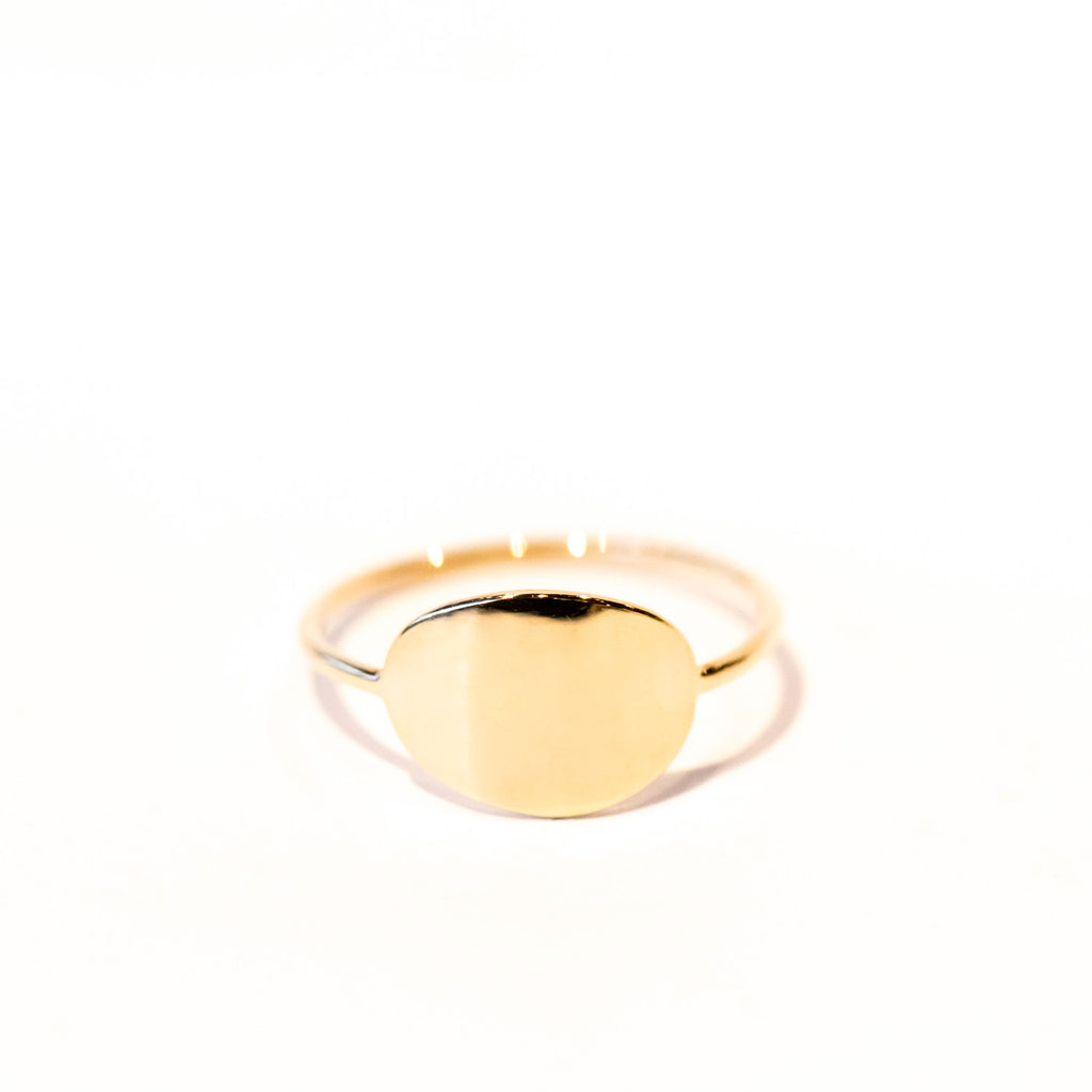 A modern gold signet ring with a thin wire band and flat oval top.