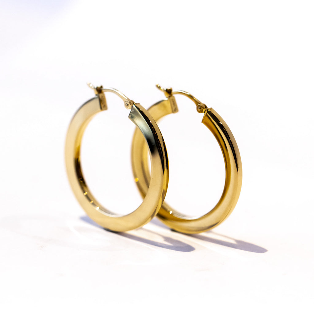 A pair of slim gold, rectangular profile hoop earrings.