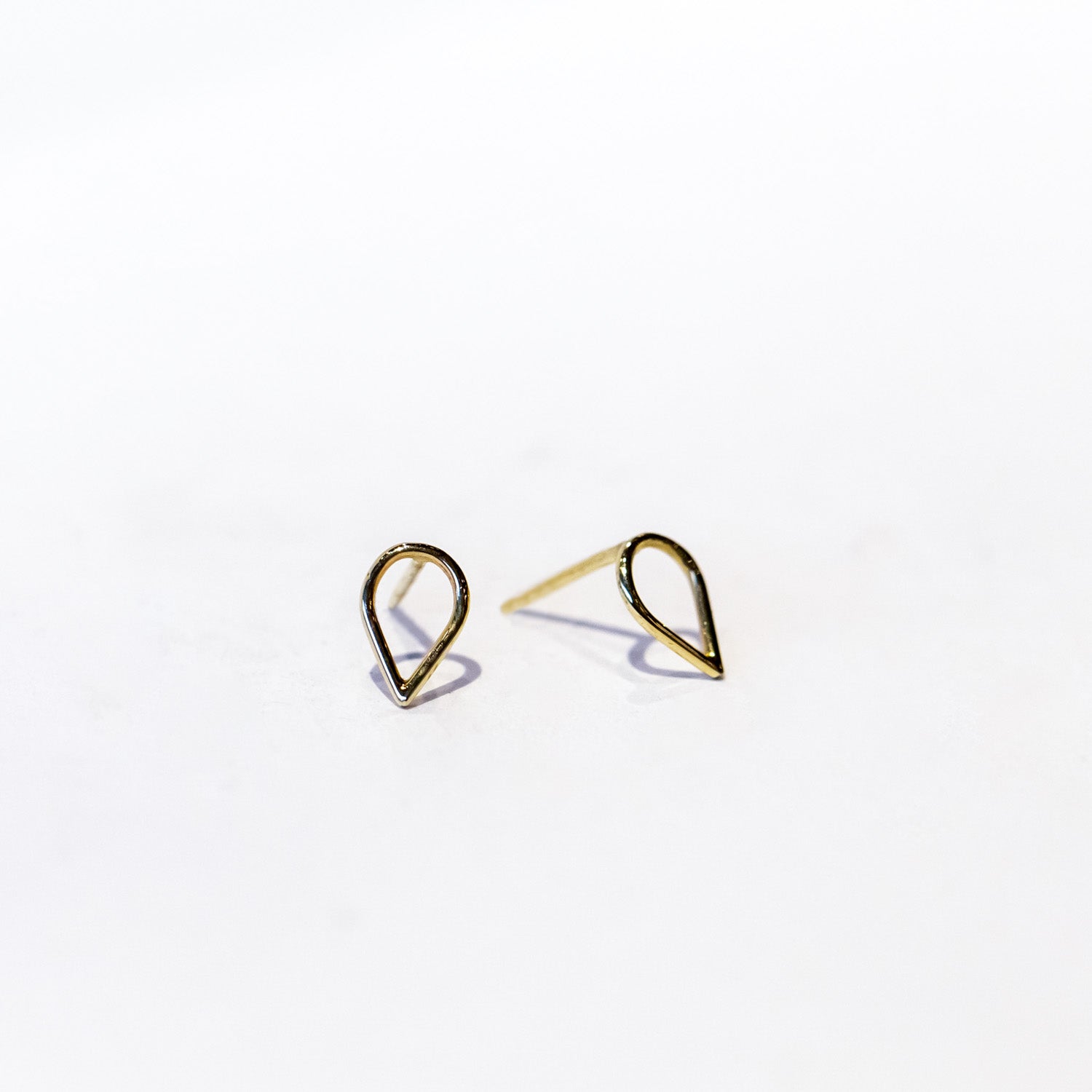 A pair of small gold stud earrings in an open teardrop outline.