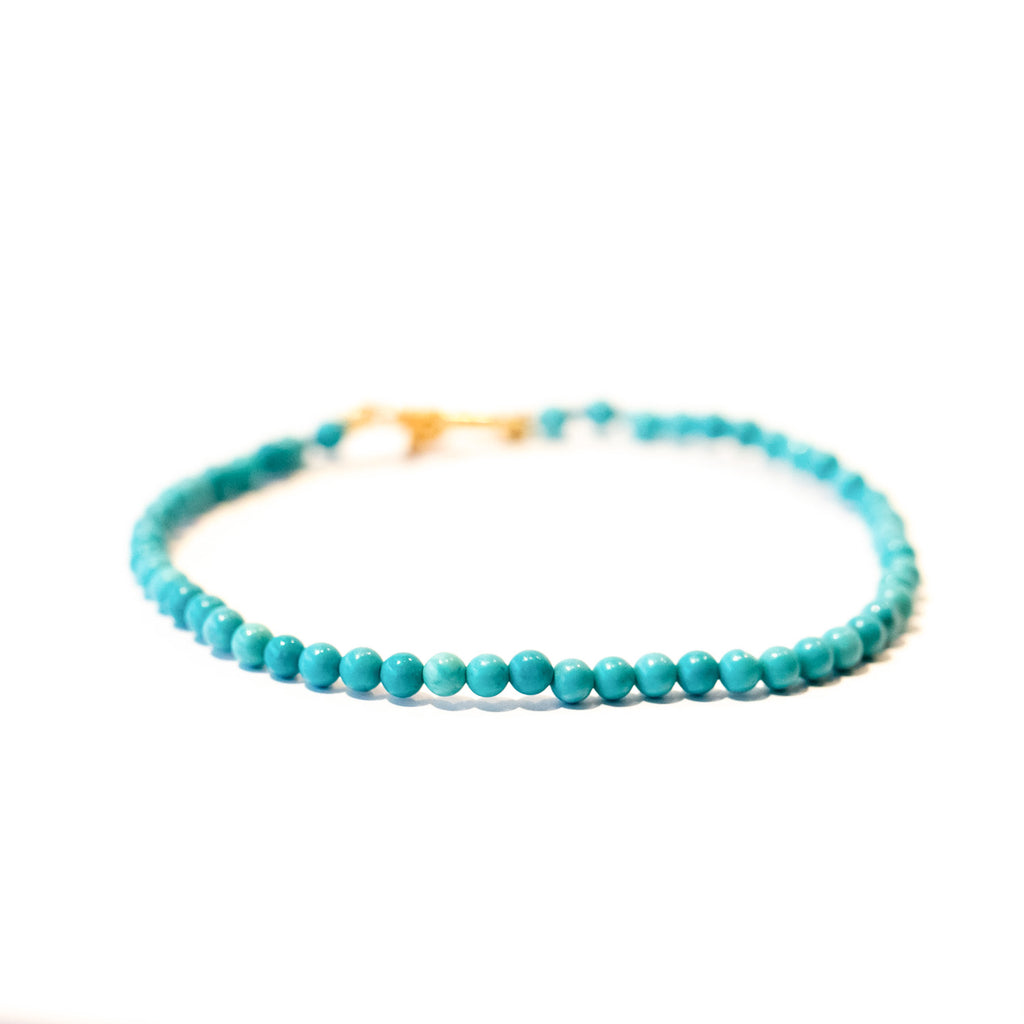 A dainty turquoise bead bracelet with gold clasp.