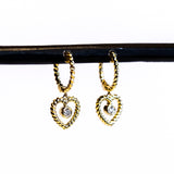 A twist-design huggie style hoop earring with a twisted wire open heart drop and a bezel set diamond dangle in the center.
