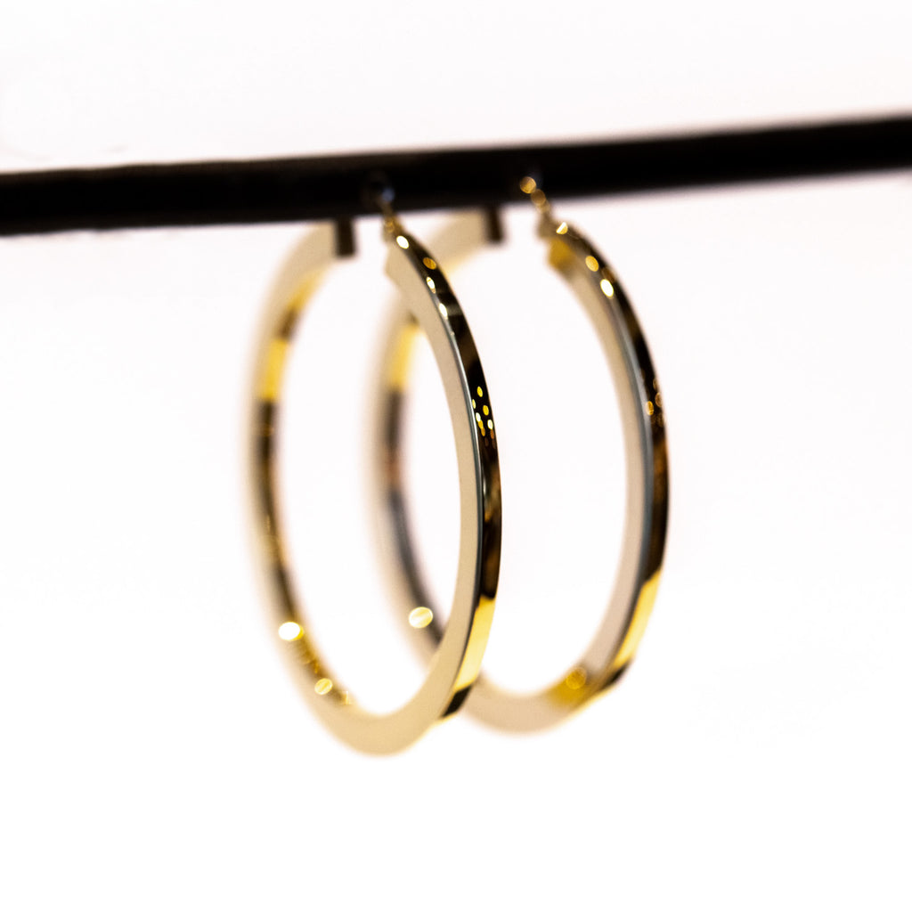 A large pair of flat profile gold hoop earrings.