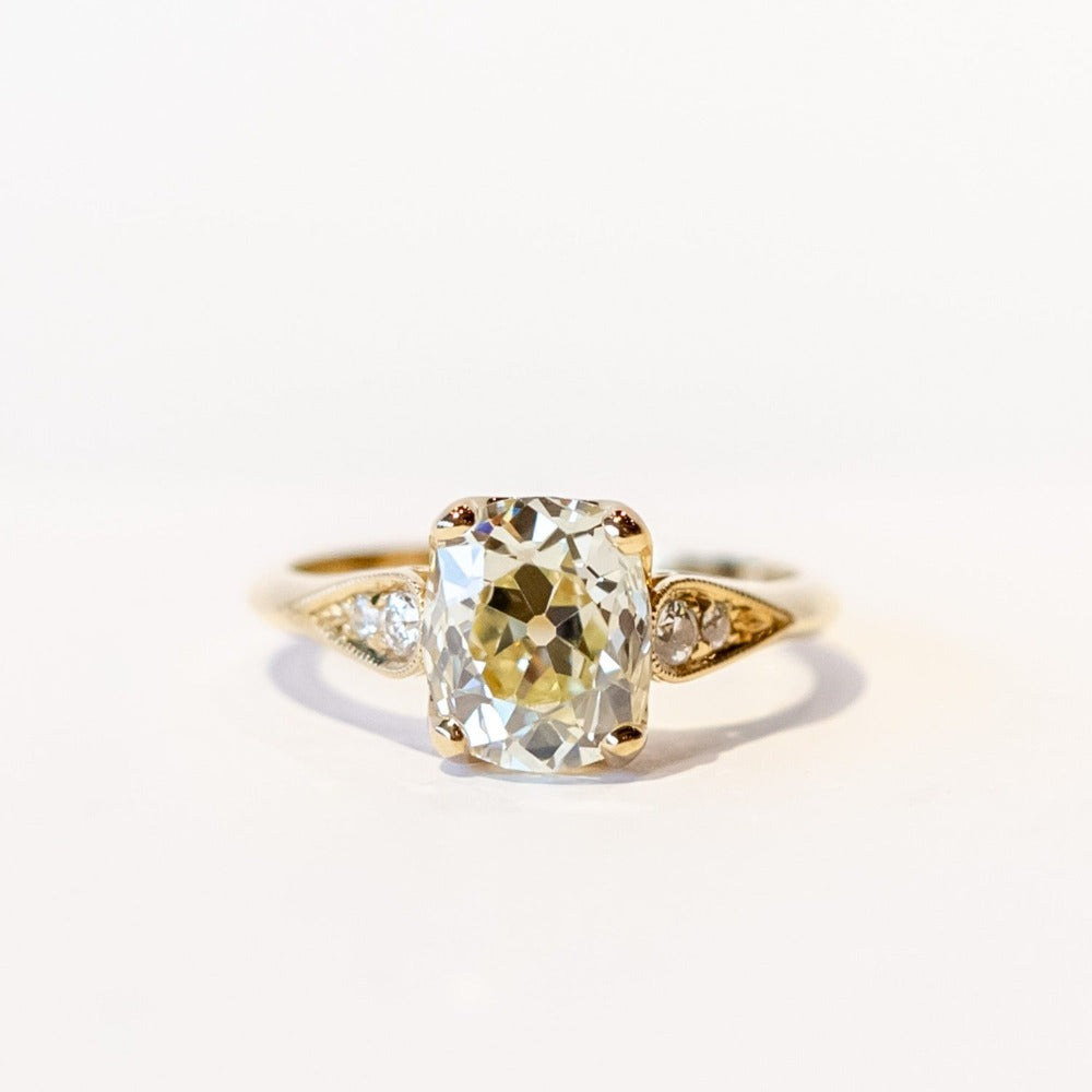 A yellow gold diamond engagement ring with a large, light yellow cushion cut diamond center stone and small accent diamonds on each shoulder.