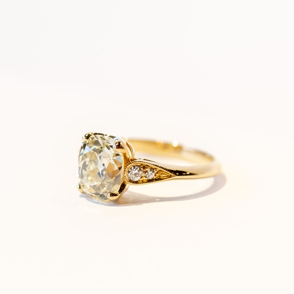 A yellow gold diamond engagement ring with a large, light yellow cushion cut diamond center stone and small accent diamonds on each shoulder.