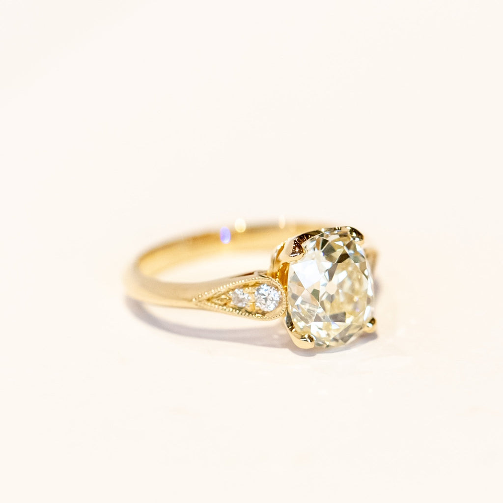 A yellow gold diamond engagement ring with a large, light yellow cushion cut diamond center stone and small accent diamonds on each shoulder.