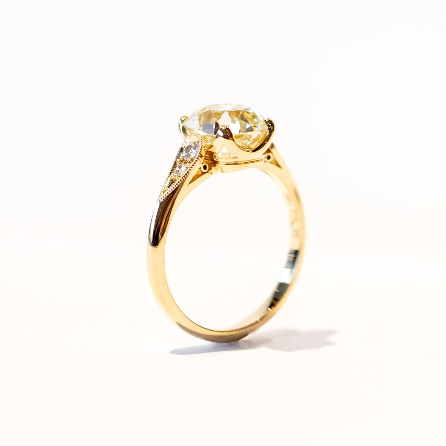 A yellow gold diamond engagement ring with a large, light yellow cushion cut diamond center stone and small accent diamonds on each shoulder.