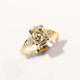 A yellow gold diamond engagement ring with a large, light yellow cushion cut diamond center stone and small accent diamonds on each shoulder.
