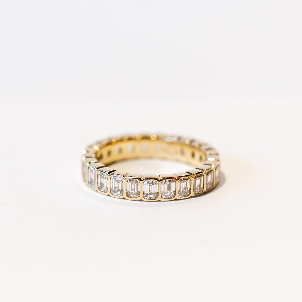 A yellow gold and diamond eternity band with bezel set emerald cut diamonds set vertically all the way around.