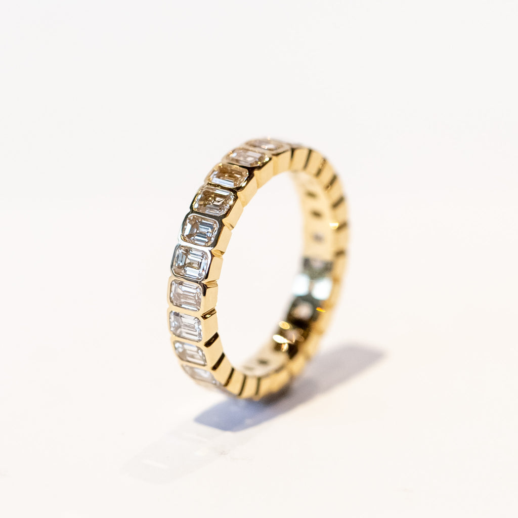 A yellow gold and diamond eternity band with bezel set emerald cut diamonds set vertically all the way around.