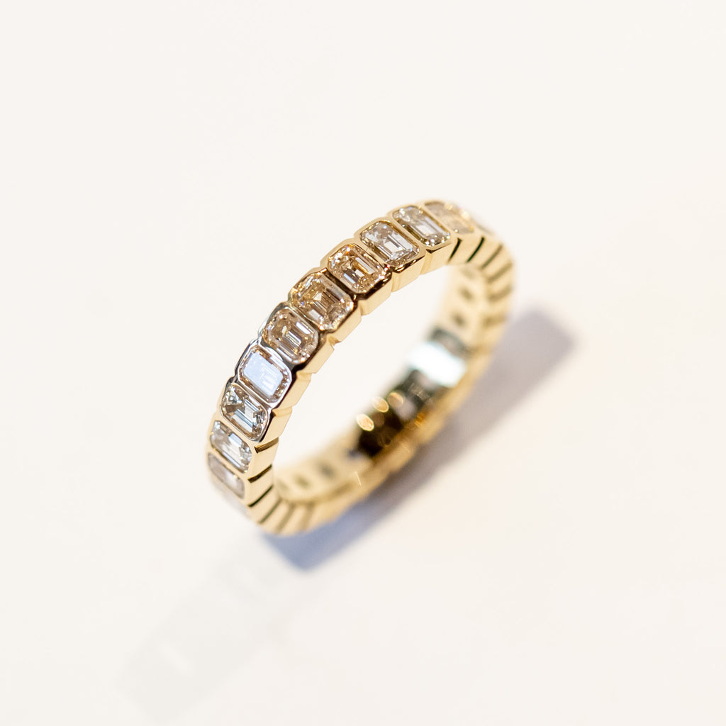 A yellow gold and diamond eternity band with bezel set emerald cut diamonds set vertically all the way around.