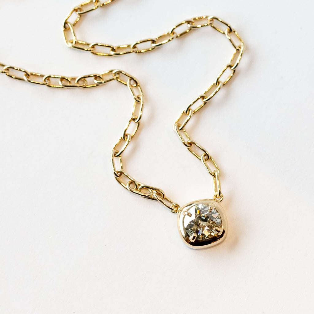 A yellow gold chain necklace of oval links with a prong set diamond on a gold cushion mounting stationed at the center.